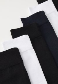 Six paires de chaussettes de couleurs : noir, blanc, bleu marine et gris foncé. Texture côtelée avec des bords élastiques. Rangées soigneusement en ligne.