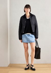 Czarna pikowana kurtka z srebrnymi guzikami, czarny sweter, jasnoniebieska spódnica dżinsowa i czarne buty na obcasie. Czarna torba na ramię w dłoni.