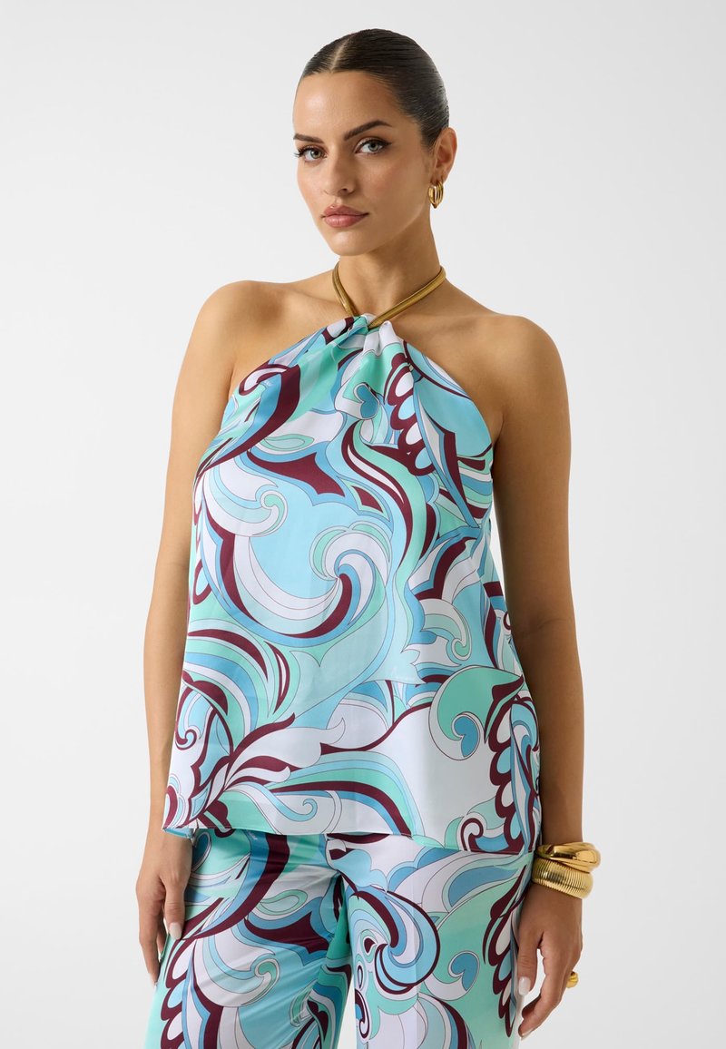 Femme portant un top dos nu et un pantalon assorti avec des motifs tourbillonnants bleu, sarcelle, blanc et bordeaux, accessoirisée de bijoux en or.