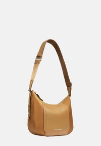 Bolso bandolera de cuero color tan con una silueta curva, correa de tela ajustable y cierre de cremallera. Presenta una marca minimalista en plata en la parte delantera.