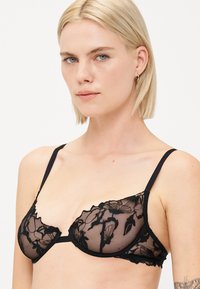 Sutien negru din dantelă, cu broderie florală, material transparent, bretele ajustabile și un design cu margine ondulată.