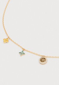 Κολιέ σε χρυσό τόνο με διάφορα φυλακτά: μια συστάδα κίτρινων λίθων, ένα τιρκουάζ λουλούδι και ένα κυκλικό μενταγιόν διακοσμημένο με διαφανείς πέτρες.