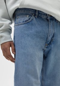 Světlé modré džíny z denimu, s klasickým designem pěti kapes, rovnými nohavicemi a jemným vyblednutím látky.