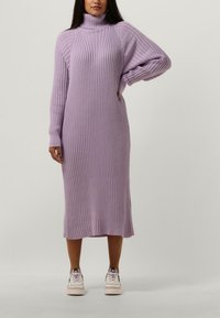Robe en maille côtelée à manches longues de couleur lavande douce, avec un col montant, des découpes latérales et une coupe décontractée, portée avec des baskets blanches.