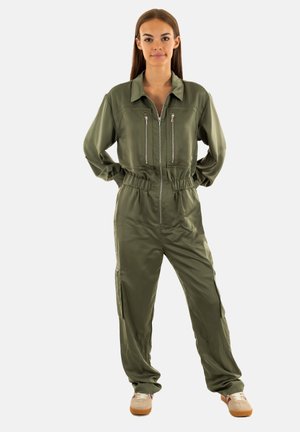 Jumpsuit verde oliva con zip frontale, due tasche sul petto con zip, vita elasticizzata e zip laterali. Tessuto leggero e liscio.