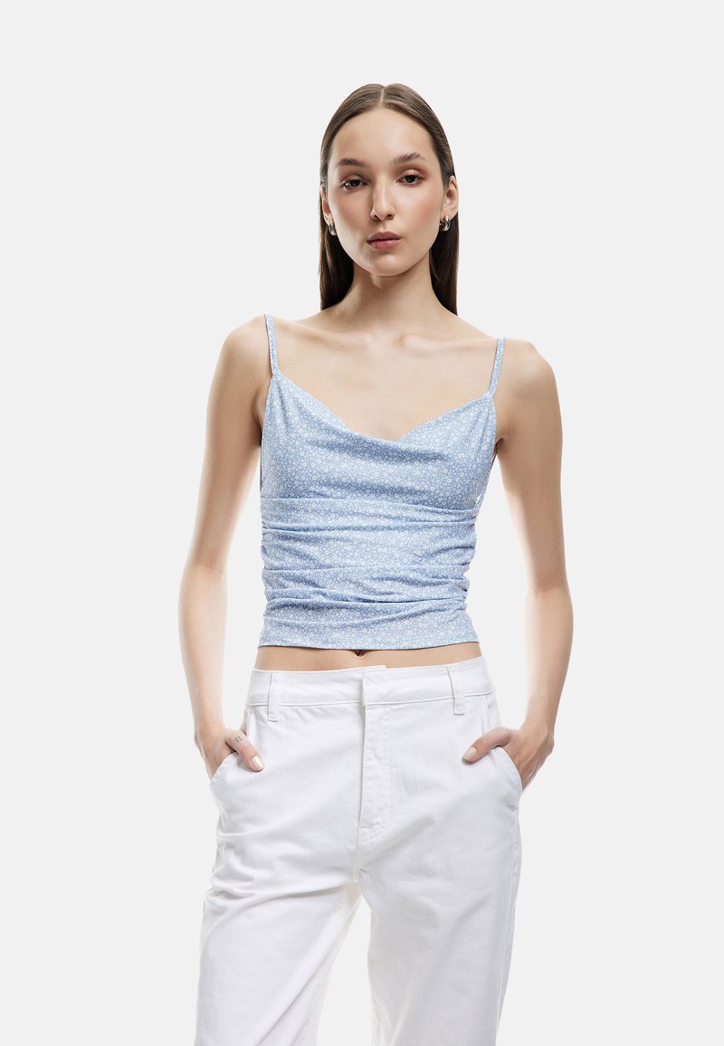 Vaaleansininen, vartalonmyötäinen toppi ohuilla olkaimilla, jossa on teksturoitu kukkakuosi ja hieman kerrottu muoto vyötäröllä.