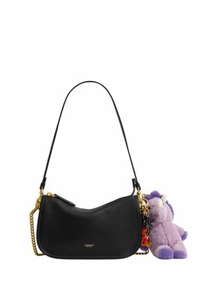Schwarze Coach-Schultertasche mit goldener Kettenriemen und lila Plüscheinhorn-Schlüsselanhänger an der Seite vor weißem Hintergrund.