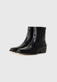 Botas de cuero negro hasta el tobillo con punta afilada, que presentan costuras intrincadas y un tacón bajo tipo bloque. Textura suave con detalles decorativos.