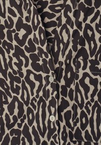 Gros plan d'un vêtement boutonné avec un motif léopard irrégulier noir et beige et une poche avant visible.