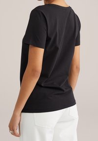 Black short-sleeve t-shirt made of smooth cotton, featuring a classic crew neck and a fitted design. Worn with white jeans.
