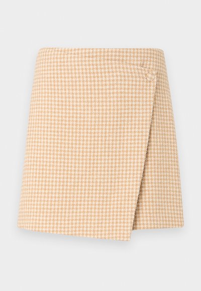Φούστα τύπου wrap με μπεζ και λευκό μοτίβο houndstooth και κουμπί στο πάνω δεξιά μέρος, εμφανίζεται σε απλό ανοιχτό φόντο.