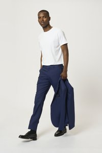 Camiseta blanca de manga corta combinada con pantalones sastre azul marino. Zapatos de vestir negros complementan el conjunto, con un blazer colgado de un brazo.