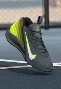 Grå atletiksko med neongrønne accenter, struktureret overdel, strømlinet design, fremtrædende hvid swoosh og en lavprofil sål.