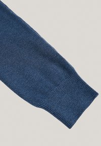 Słonikowy niebieski sweter z dzianiny, z rękawem, który ma teksturowany wzór i ściągacz na końcu. Materiał wydaje się miękki i ciasno tkany.