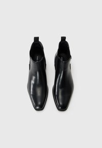 Botas de tobillo de cuero negro con un acabado brillante, punta afilada, recortes laterales y una pequeña lengüeta en la parte posterior. Diseño minimalista.