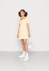 Vestido floral amarelo com mangas bufantes e corpete ajustado. Botas de combate brancas com atacadores e uma pequena mala branca como acessórios.