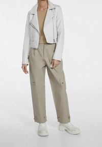 Vit läderbikerjacka över en guldglittrig topp, parat med beige cargobyxor med fickor och vita chunky sneakers.