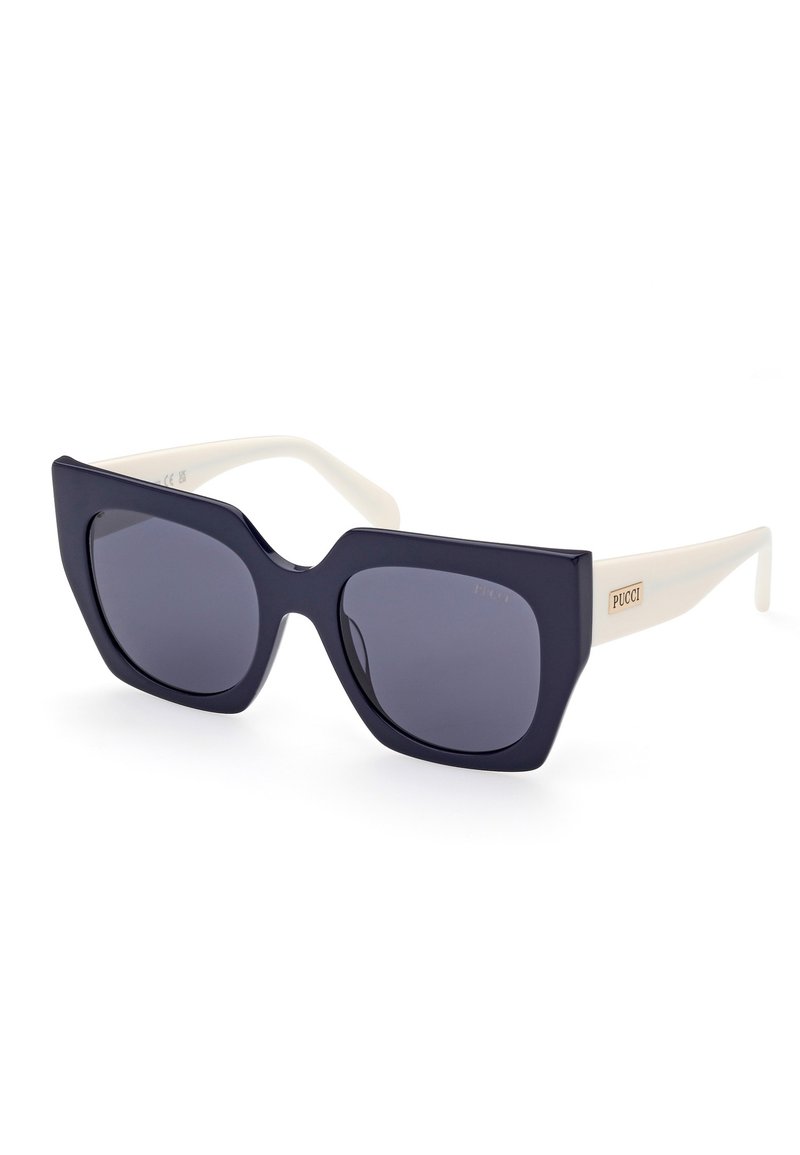 Navy blue oversized sunglasses with a distinctive angular shape, featuring dark lenses and cream-colored arms with a gold logo accent.