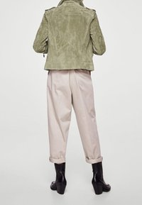 Olivgrüne Wildlederjacke mit strukturiertem Design, kombiniert mit hellbeigen Hosen mit umgekrempelten Säumen und schwarzen Stiefeletten mit Absatz.