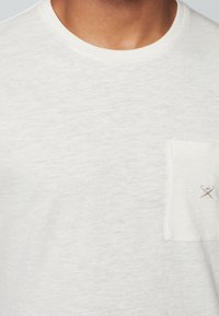 Męska biała koszulka typu crew neck z teksturowanym wykończeniem, z lewą kieszonką na piersi i małym haftowanym wzorem w rogu.