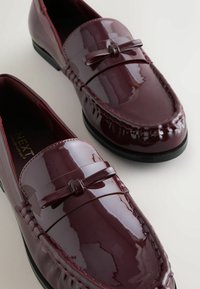 Burgunderfarbene Lacklederloafers mit einem gestickten Design und einem dekorativen Schleifenakzent an der Vorderseite. Schwarze Gummisohle für besseren Halt.