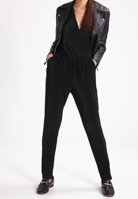 Svart byxdress med vertikal ribbad textur, v-ringning, insvängda ben och elastisk midja, i kombination med en svart skinnbikerjacka och loafers.