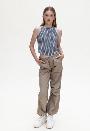 Cropped haltertop in marineblauw met een wit stippenpatroon; lichte, beige, high-waisted broek; witte sneakers. Minimalistisch ontwerp en een ontspannen pasvorm.