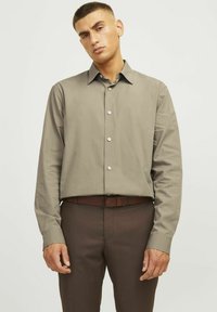 Shirt: lange mouwen, licht grijs-bruin stof, klassieke kraag, knoopsluiting aan de voorkant. Gepaard met donkerbruine broeken, aangevuld met een bijpassende riem.