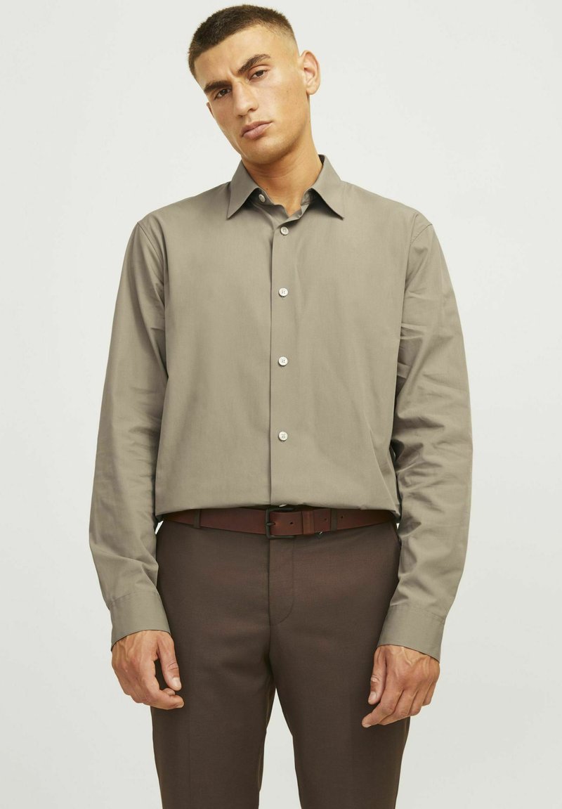 Shirt: lange mouwen, licht grijs-bruin stof, klassieke kraag, knoopsluiting aan de voorkant. Gepaard met donkerbruine broeken, aangevuld met een bijpassende riem.