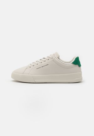 Lichtbeige sneaker met een glad leren bovenwerk, groene suède hielaccent, platte veters en een minimalistische rubberen zool. Logo weergegeven aan de zijkant.
