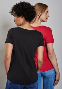 Dos camisetas exhibidas de espaldas: una negra con escote amplio y la otra roja, ambas hechas de una tela suave y con mangas cortas.