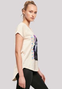 Cremefarbiges T-Shirt mit kurzen Ärmeln und einem bedruckten Design, das einen Charakter aus "The Witcher" zeigt. Ausgestellter Saum und weicher Stoff.