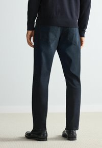 Donkerblauwe jeans met een rechte pijp, zakken met stikdetails en een gladde stoftextuur, gecombineerd met zwarte schoenen.