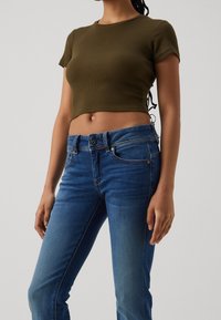 Top corto de canalé en verde oliva con escote redondo, combinado con jeans de mezclilla azules que presentan un diseño clásico de cinco bolsillos y un ligero desgastado.