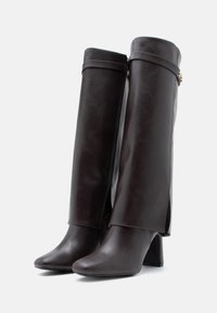 Brązowe skórzane botki na wysokim obcasie z ostrym noskiem, do kolan, z zapięciem na zamek i szeroką górną klapą z dekoracyjnym okuciem.