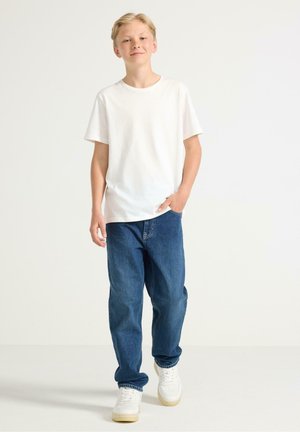 Vit kortärmad t-shirt, lösa blå jeans och vita sneakers. Outfiten har en avslappnad passform med en lätt struktur och enkel design.