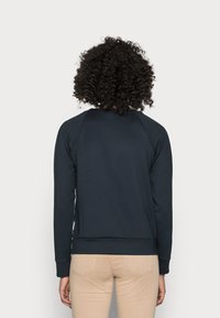 Námořnicky modrá mikina se dlouhými raglánovými rukávy, žebrovanými manžetami a lemem. Vyznačuje se hladkou texturou a jednoduchým, klasickým designem.