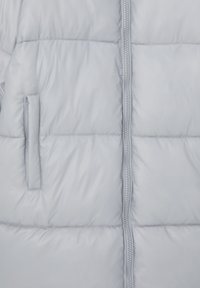 Chaqueta acolchada gris claro con una textura suave y brillante. Presenta costuras verticales, un cierre central y un bolsillo externo en la izquierda.