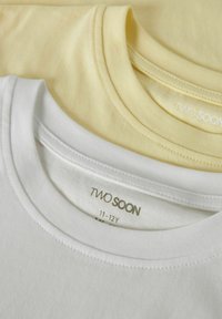 Kaks valget ja kahvatukollast voltis puuvillast T-särki suuruses 11-12 aastat, virnas, nähtavate ümara kaelusega ja brändisiltidega.