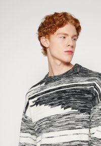 Maglione a maglia bianco e nero con un motivo testurizzato, caratterizzato da un colletto a girocollo e strisce orizzontali di diverse dimensioni. Tessuto morbido e casual.