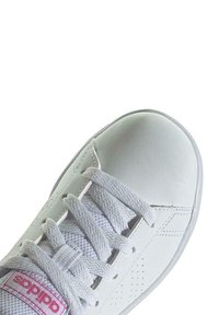 Zapatilla deportiva blanca con parte superior de cuero texturizado, cordones planos y punta redondeada con acentos perforados.