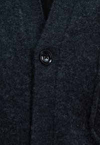 Dunkelgrauer Wollcardigan mit strukturiertem Finish, ausgestattet mit einem schwarzen Knopf und einem V-Ausschnitt-Design. Weiches Material und klassische Passform.