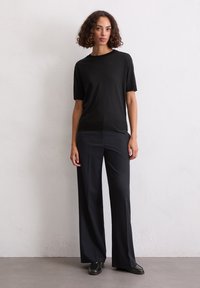 T-shirt nera a maniche corte realizzata in tessuto morbido, abbinata a pantaloni scuri a gamba larga a vita alta, con scarpe nere lucide.