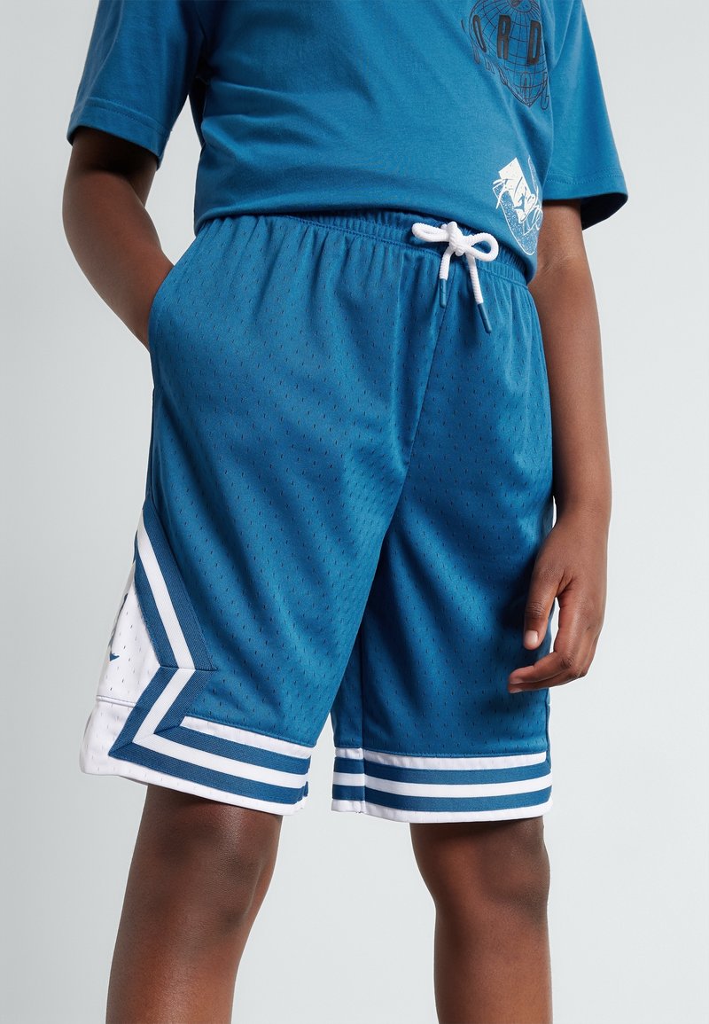 Jeune personne portant un short de basket bleu avec des rayures blanches et un cordon, assorti à un t-shirt bleu assorti.