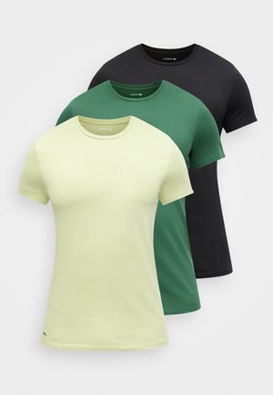 Tres camisetas Lacoste de manga corta con cuello redondo en amarillo claro, verde y negro, apiladas con los logotipos en el dobladillo inferior izquierdo.