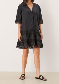 Černé šaty s krátkými rukávy, véčkovým výstřihem, krajkovým lemem na spodním okraji a rukávech, s vrstevnatým designem, vyrobené z lehkého materiálu. V kombinaci s černými sandály.