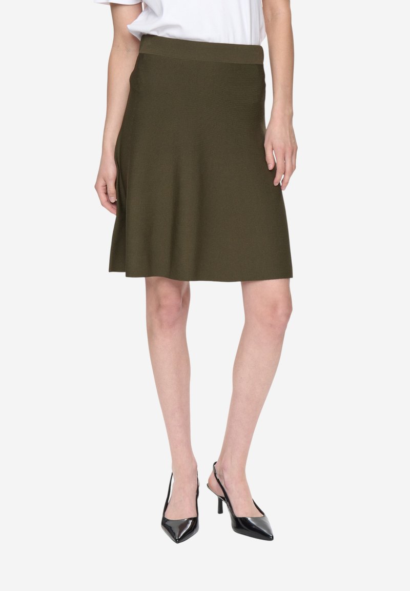 Jupe trapèze vert olive en tissu tricoté texturé, dotée d'une large ceinture et d'une longueur mi-cuisse. Associée à des chaussures à talons noires.