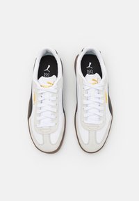 Vita sneakers med mocka- och läderöverdrag, med snörning, svart foder och en brun gummisula. Inkluderar detaljer med guldlogo.