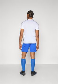 Sportsoutfit med en hvid kortærmet skjorte, blå shorts, blå sokker og sorte fodboldstøvler, set fra ryggen.