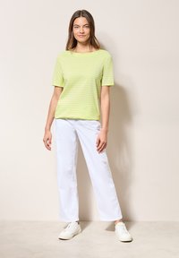 Tričko s krátkým rukávem pruhované v limetkově zelené barvě, spárované s bílými širokými kalhotami a bílými teniskami. Hladká tkanina, uvolněný střih.